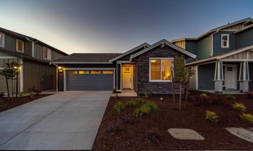 a single story home with woodchip yard and long driveway at dusk